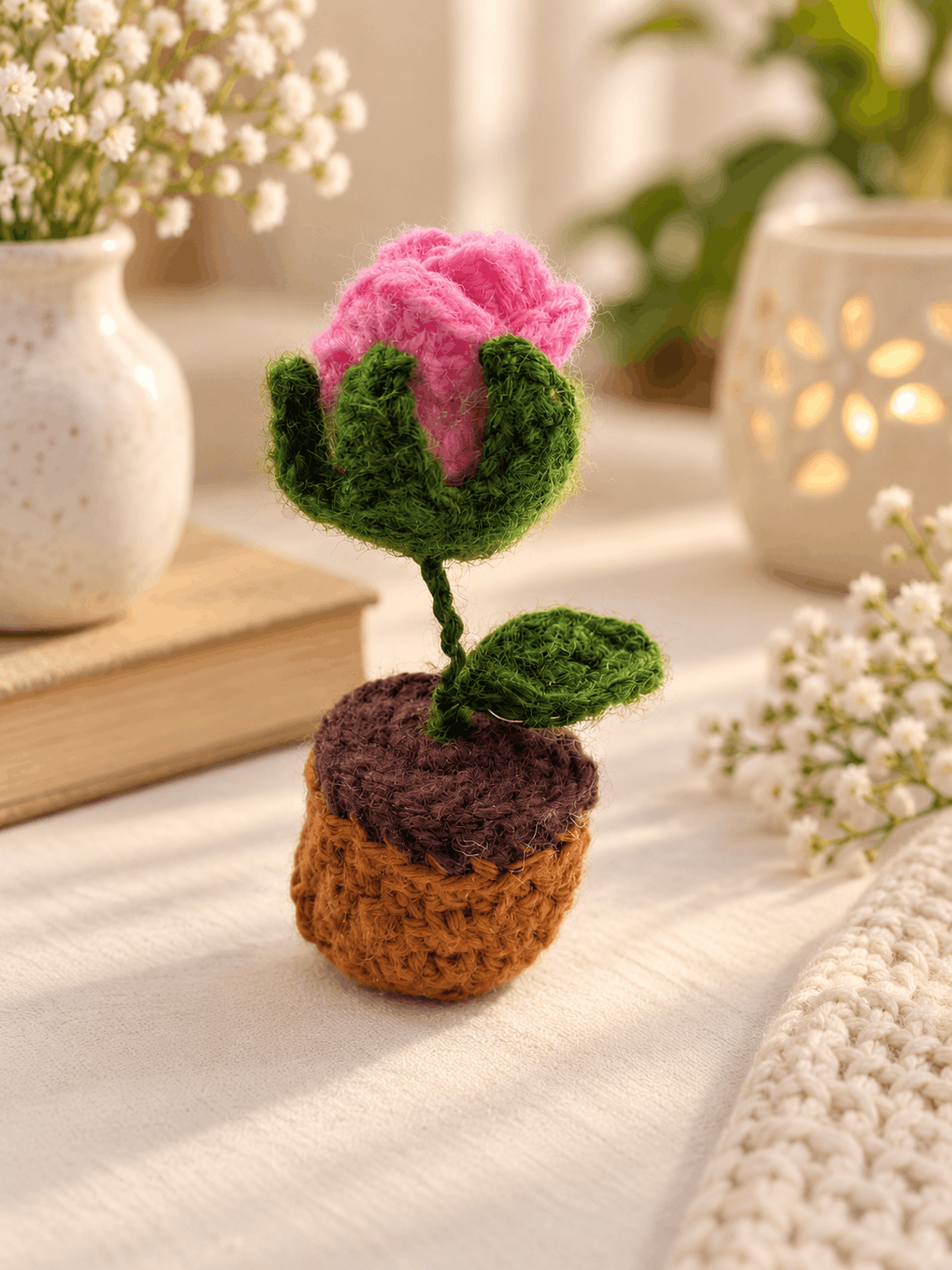 The finished crochet rose in its terracotta pot, beside a book and a candle