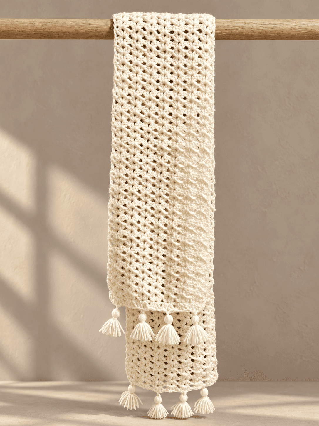 The cream lace scarf hung over a wooden rail, with both tasselled ends falling one in front of the other